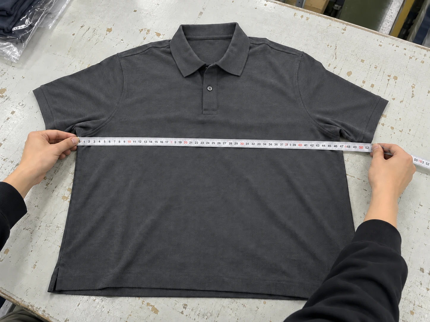 Illustrative flat chest-width measurement on a gray polo garment