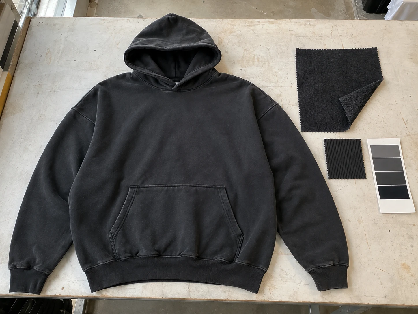 Dark pullover hoodie laid flat beside a main fabric swatch, rib reference and shade card