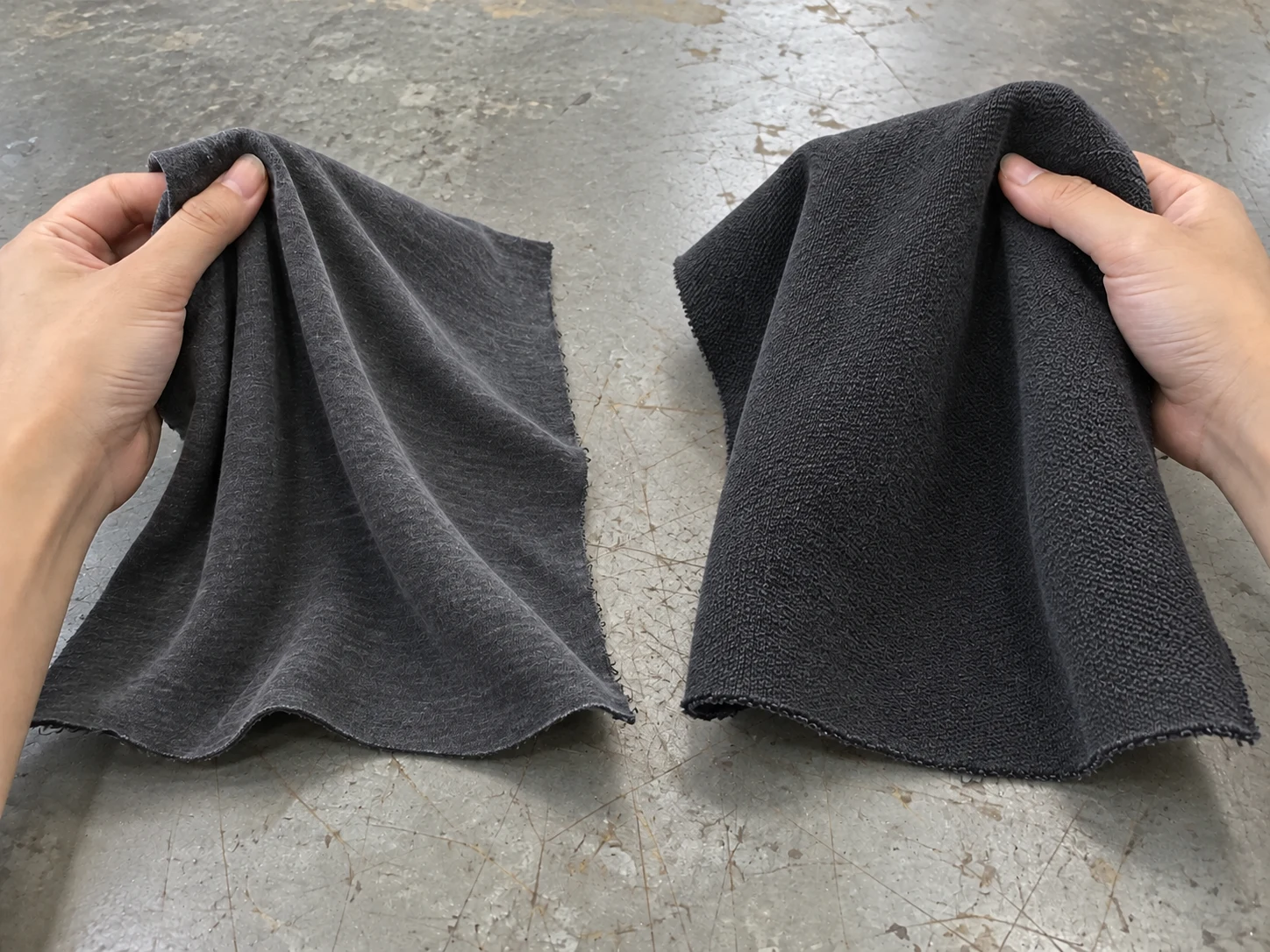 Hands lifting two dark knit swatches to show folds, drape and surface texture