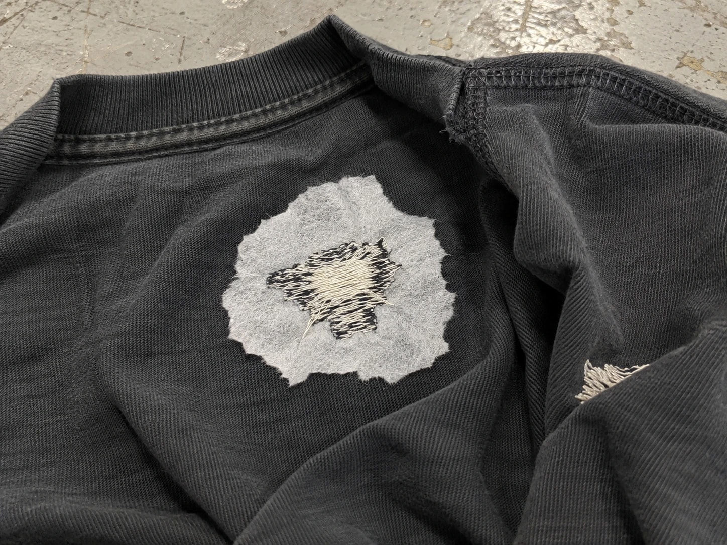 Inside of a dark T-shirt showing embroidery reverse stitches and a light-colored backing layer