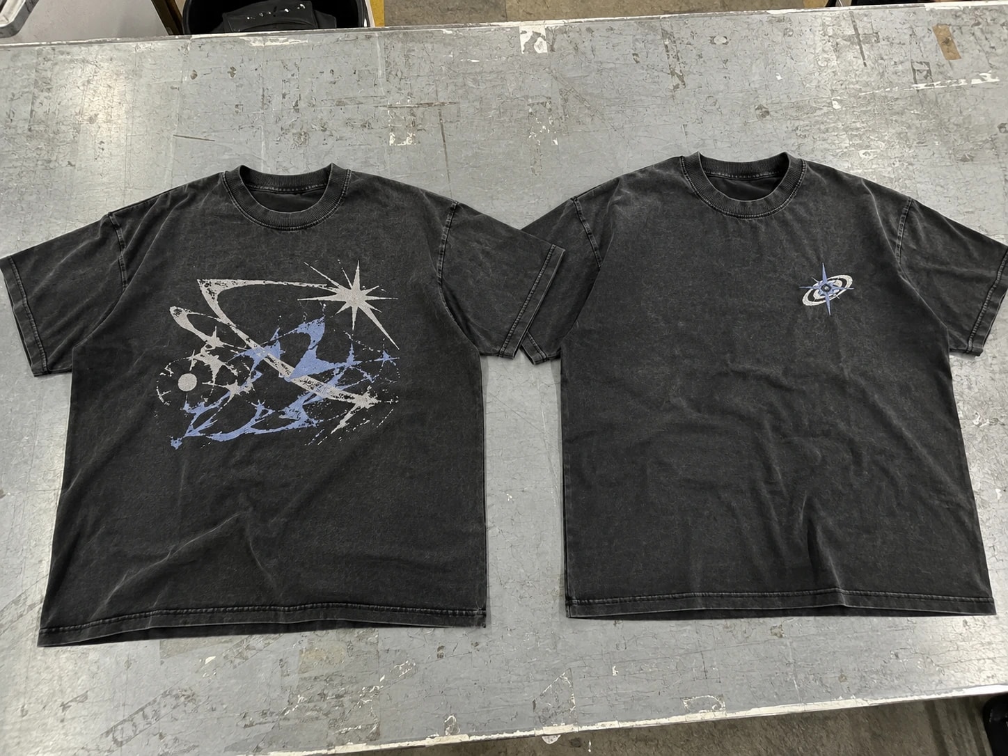Two washed dark T-shirts laid flat with a large graphic on the left and a small chest graphic on the right