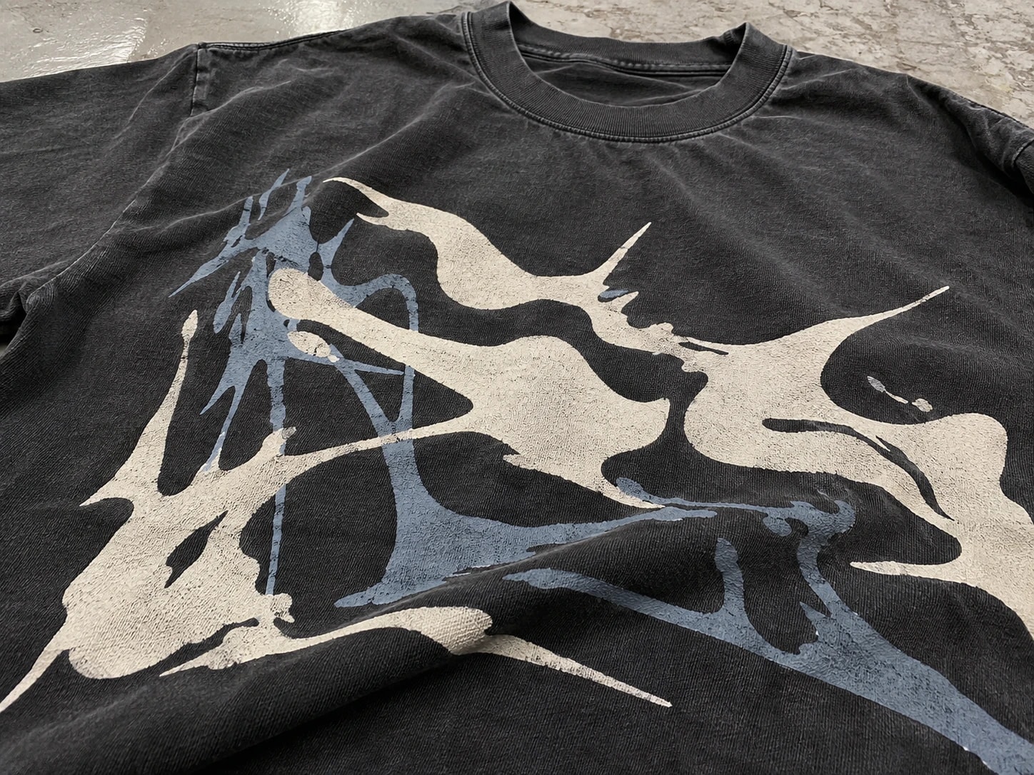 Large cream and blue screen-printed graphic on a washed dark T-shirt
