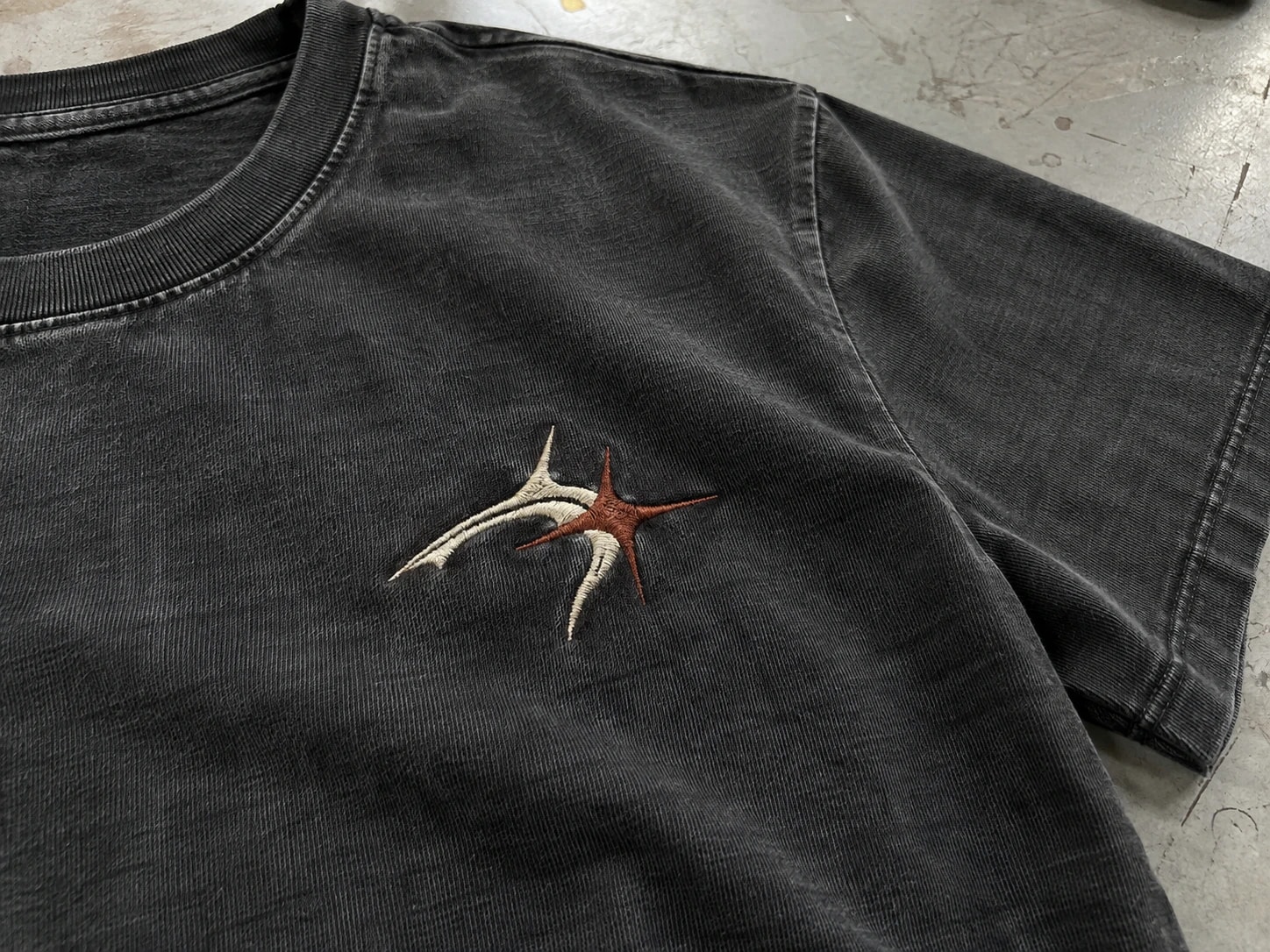 Cream and rust-colored stitched logo on a washed dark T-shirt