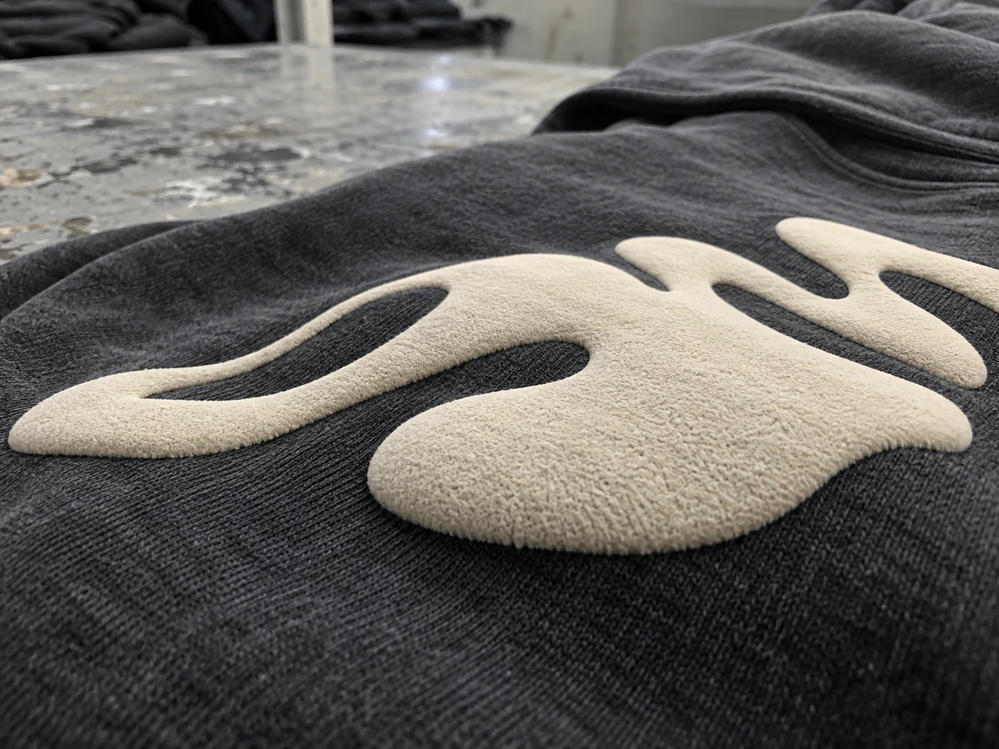 Low-angle detail of a raised cream puff print on a washed dark hoodie