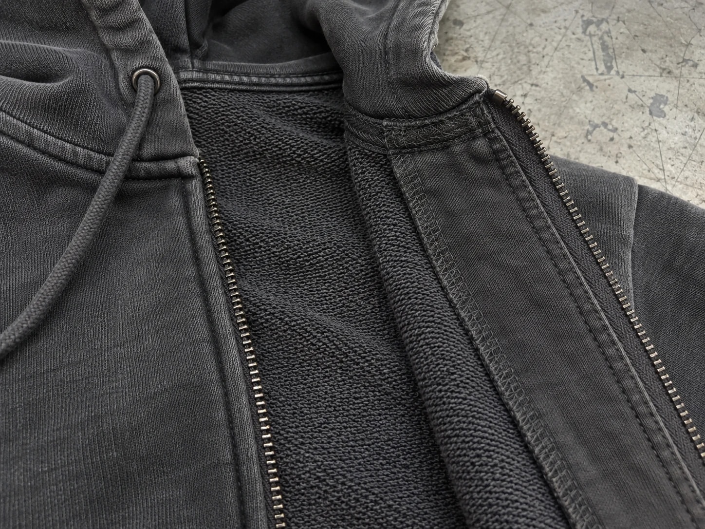 Opened dark hoodie showing inside zipper attachment, seam finishing and hood-to-neck connection