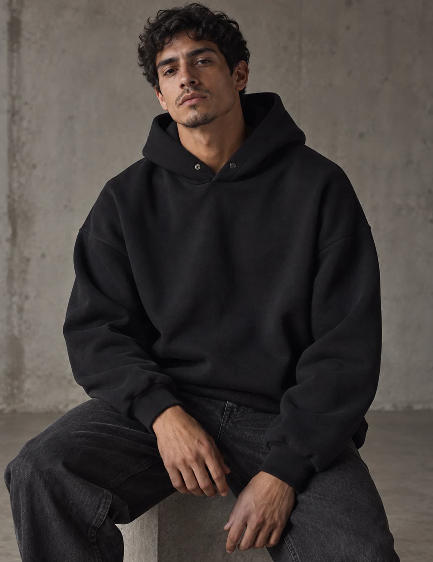 Male model wearing a clean black oversized pullover hoodie with structured hood