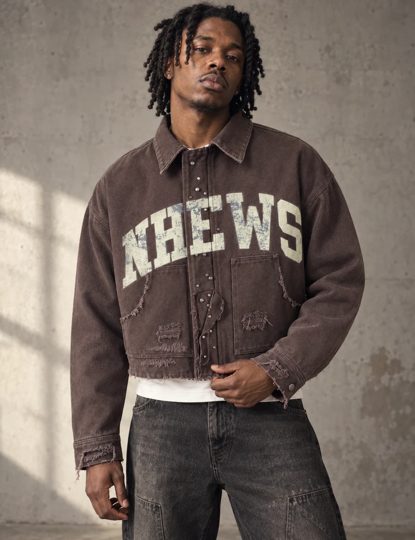 Male model wearing a brown cropped graphic workwear jacket with distressed patch pockets