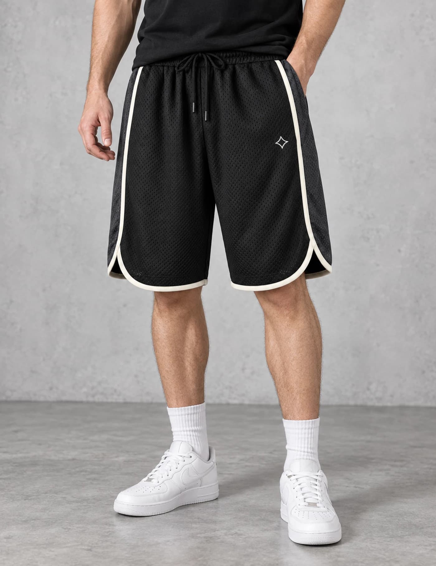 Male lower-body model wearing black basketball shorts with cream contrast binding and curved side notches