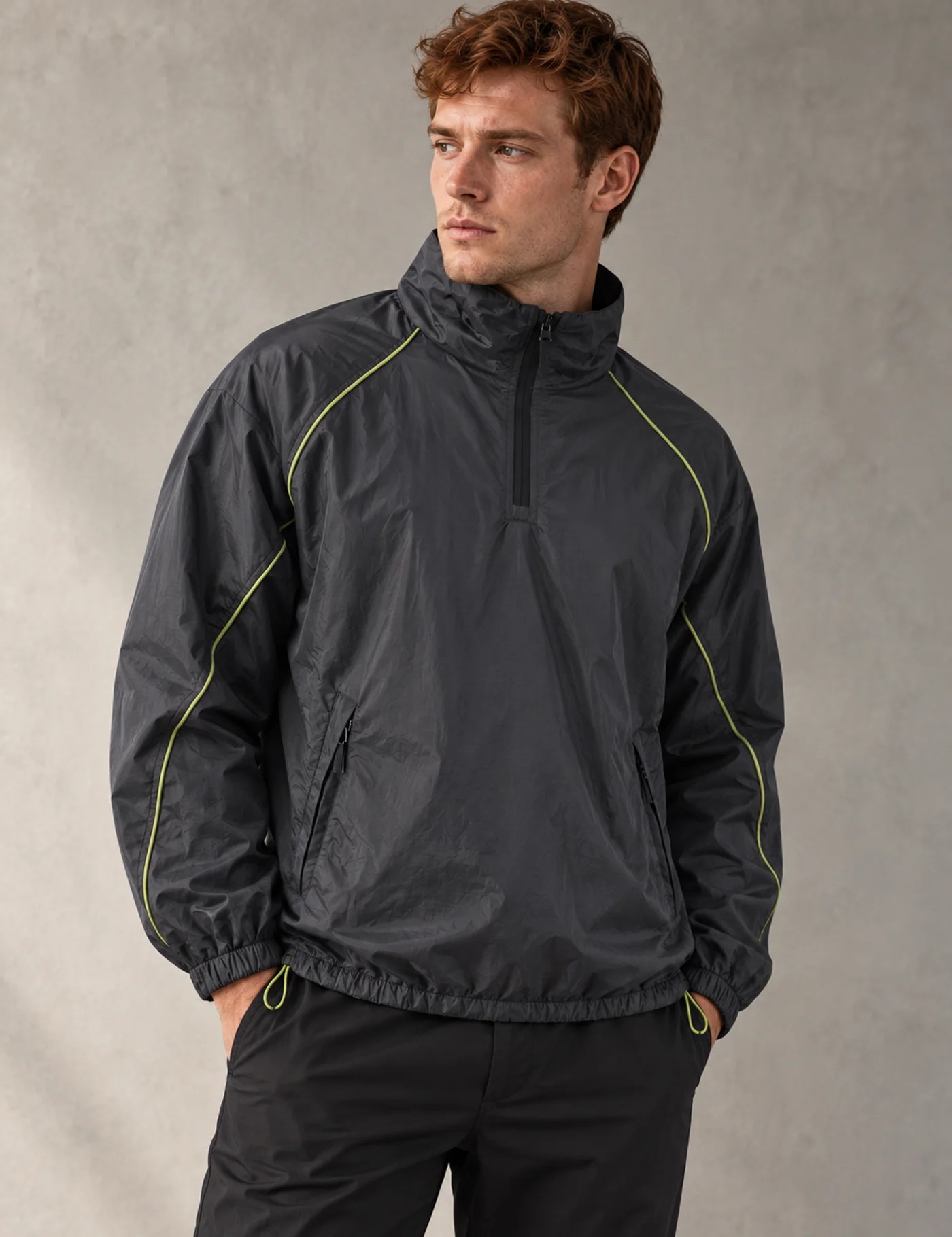 Auburn-haired European male model wearing a charcoal half-zip windbreaker with lime piping