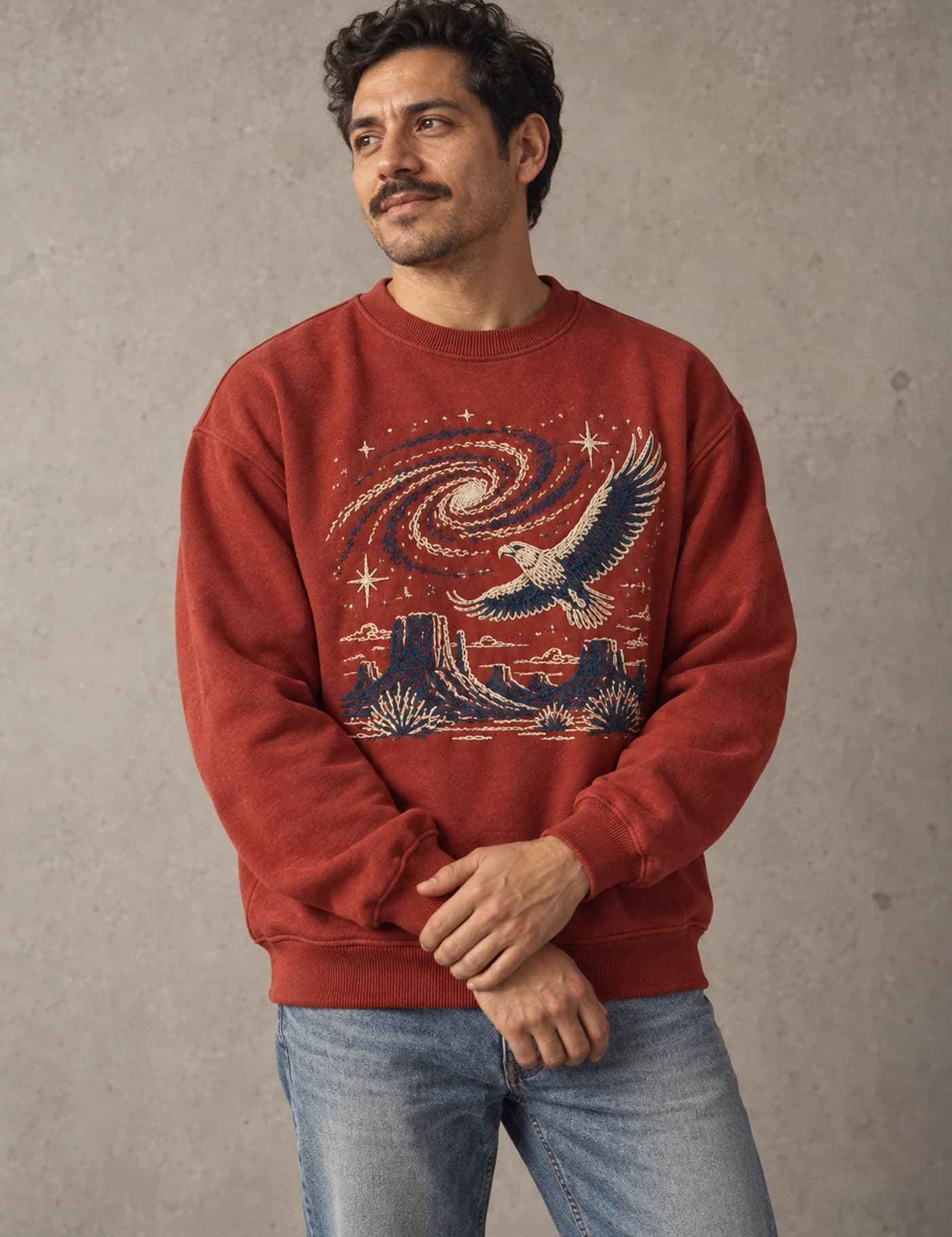 Male model wearing a red crewneck sweatshirt with large multicolor eagle and desert embroidery