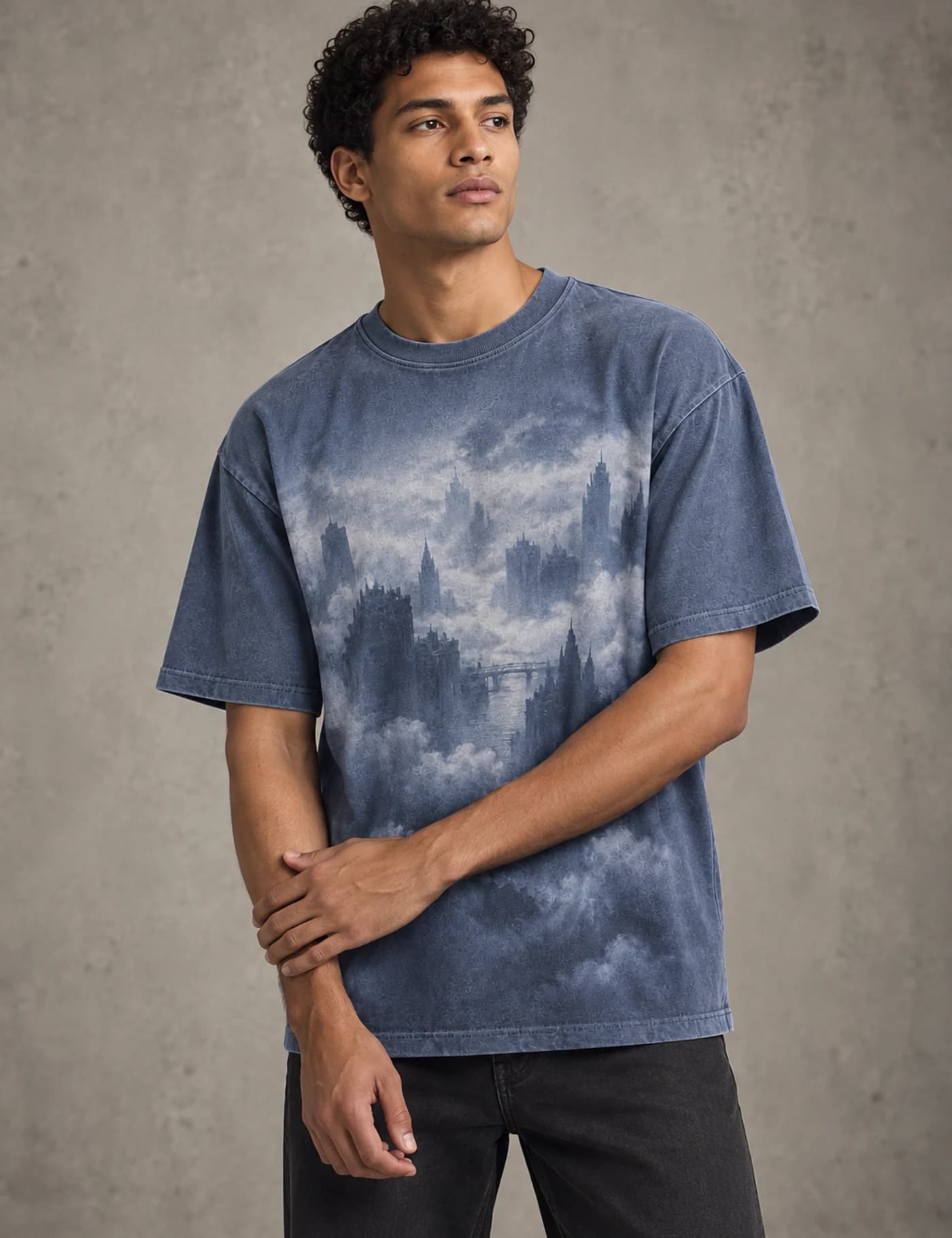 Male model wearing a washed blue oversized T-shirt with a large tonal city and cloud photographic graphic