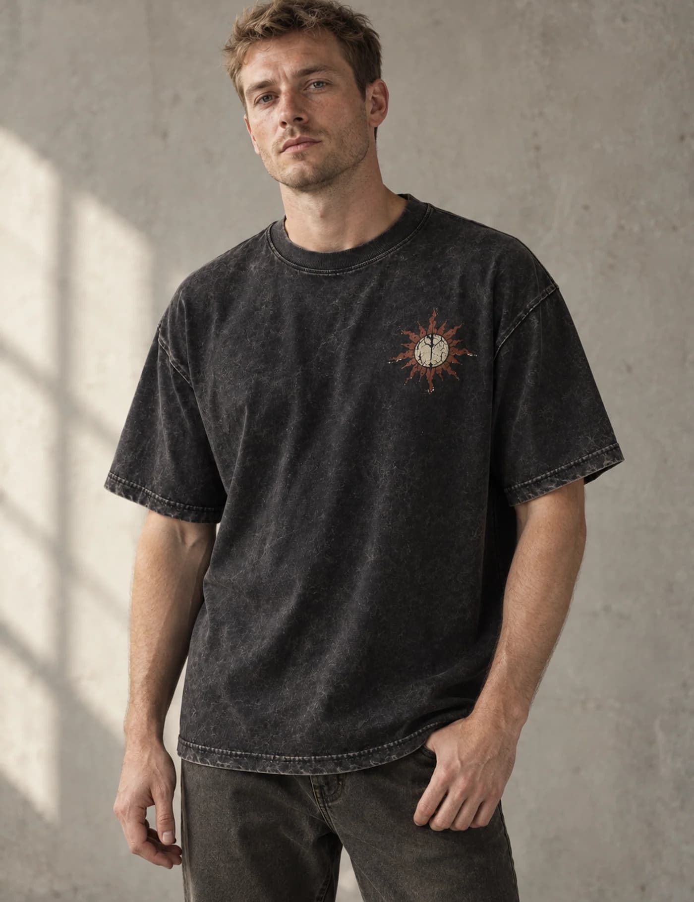 Male model wearing a washed black oversized T-shirt with a small sun chest motif and cracked back print