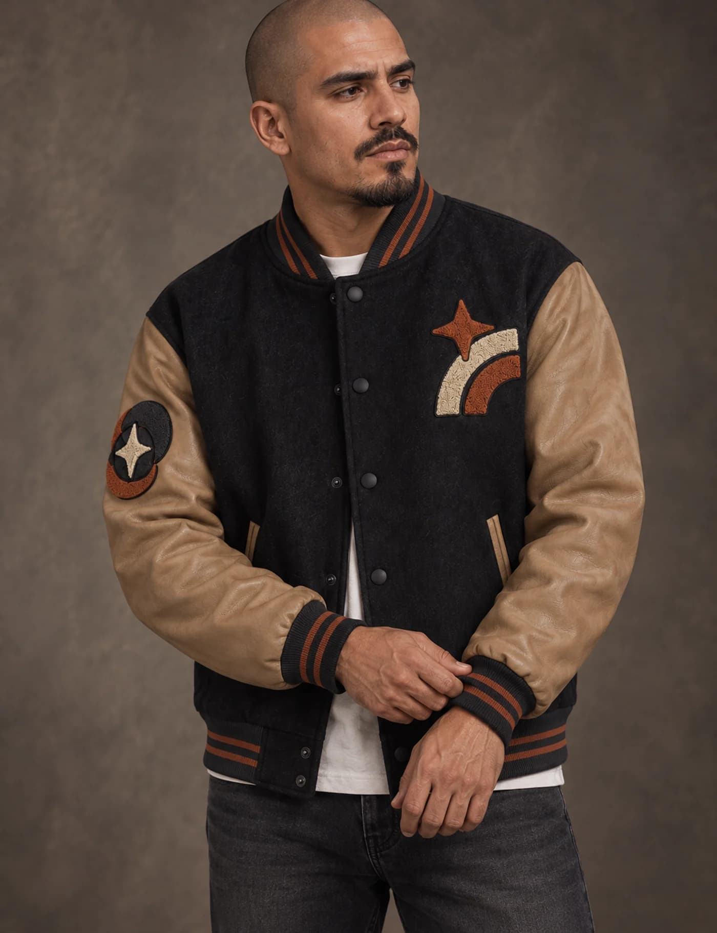 Latino male model wearing a black and tan embroidered patch varsity jacket