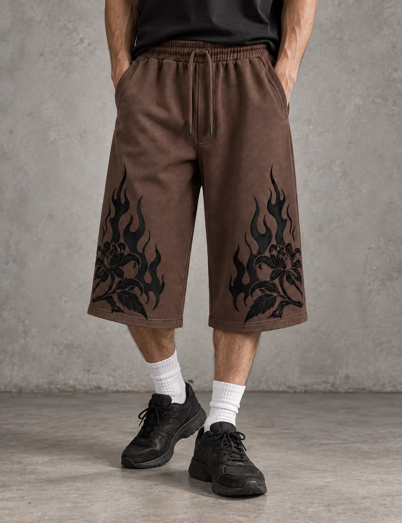 Male model wearing brown longline shorts with black flame graphics at the hems
