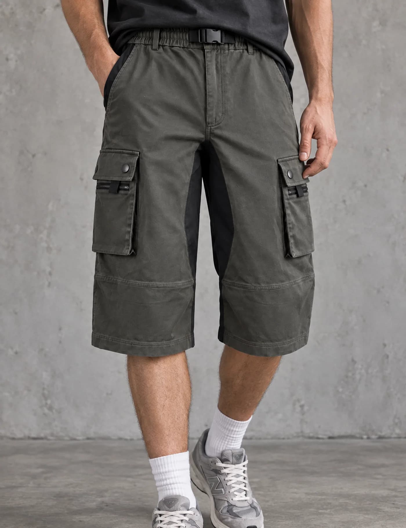 Male lower-body model wearing charcoal olive long cargo shorts with a black buckle belt