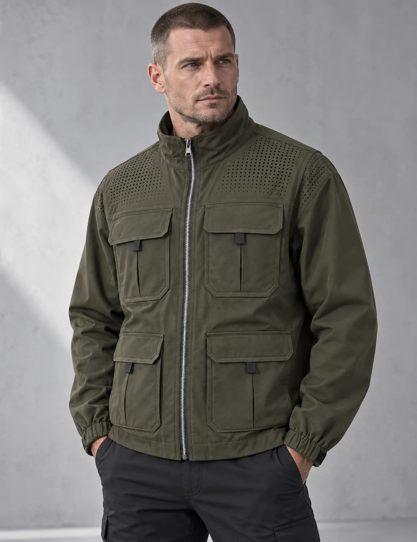 Slavic male model wearing a dark olive four-pocket stand-collar utility jacket with a perforated shoulder yoke