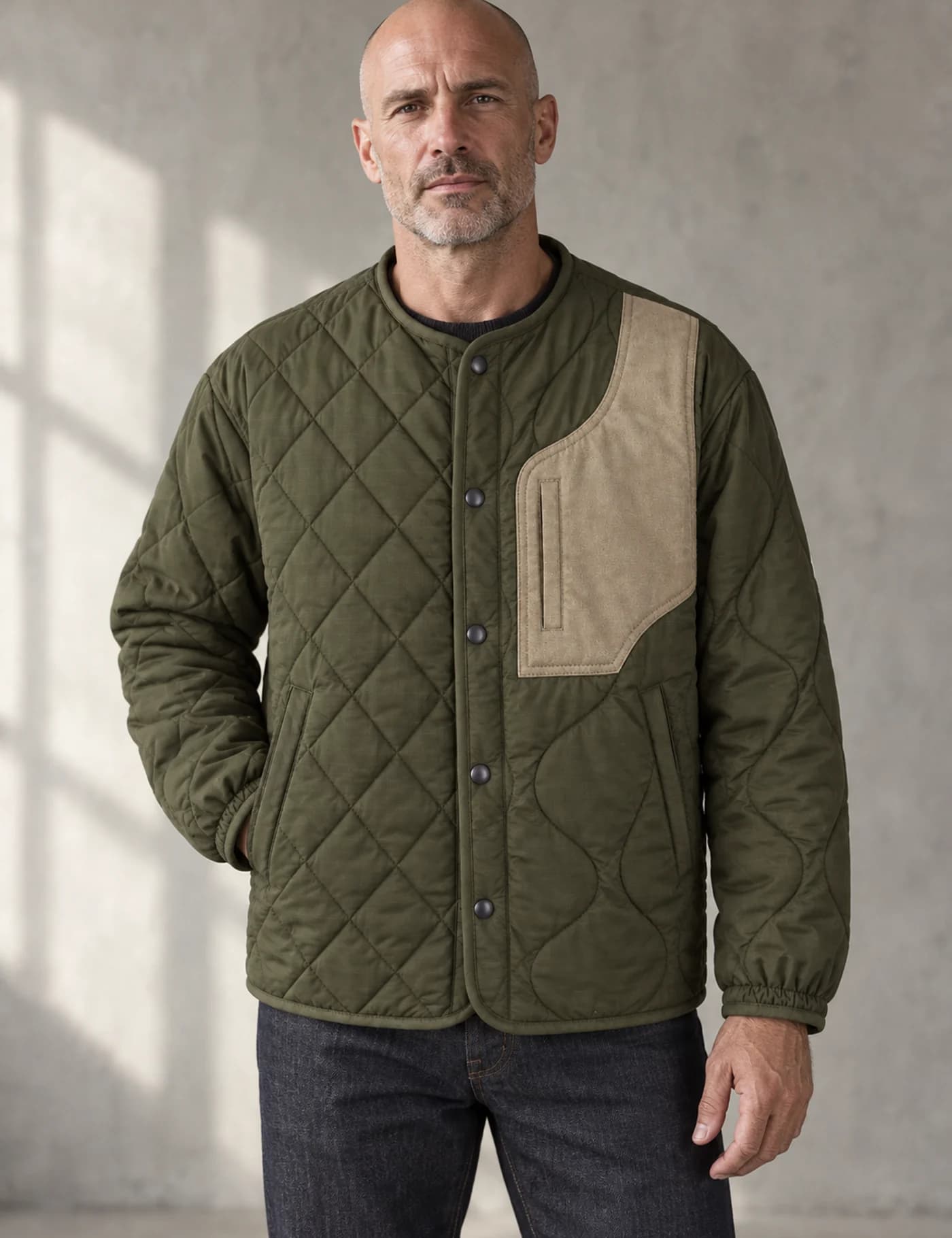 Bald male model wearing an olive quilted patchwork workwear jacket