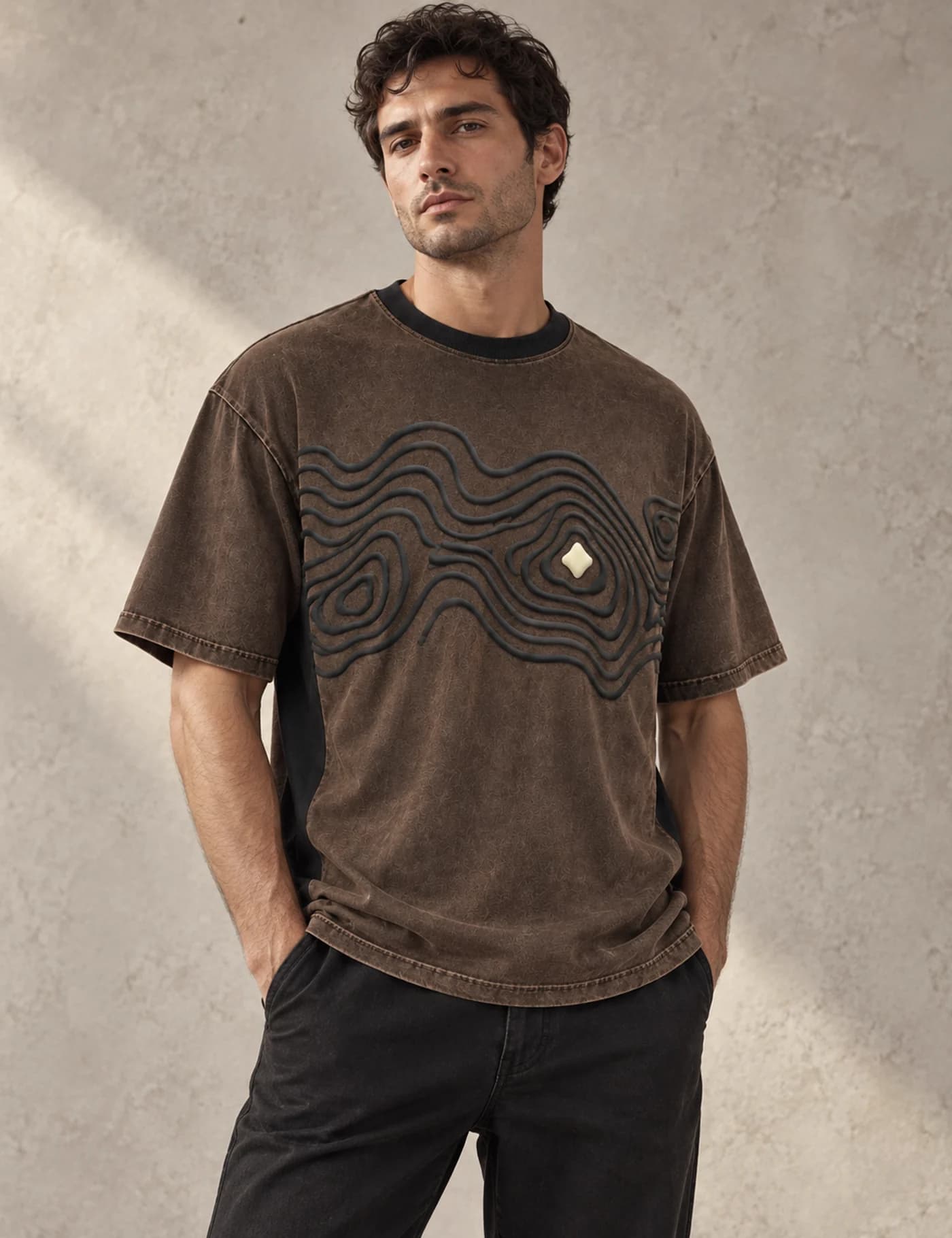 Mediterranean male model wearing a washed brown oversized T-shirt with dimensional raised cord artwork