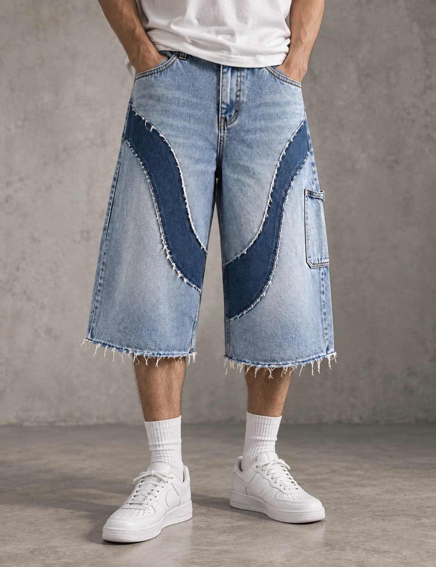 Male model wearing light-wash long denim jorts with dark curved raw-edge appliqué panels
