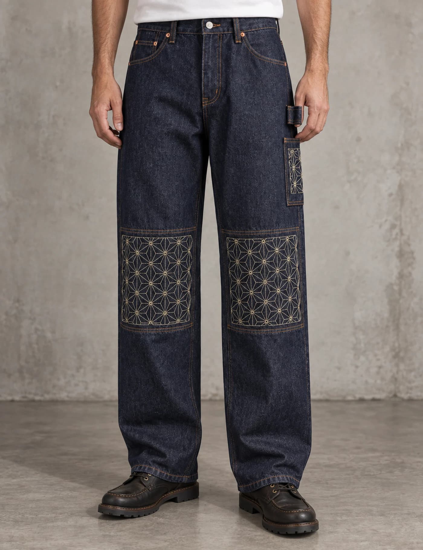 Male model wearing dark indigo utility jeans with geometric sashiko knee panels