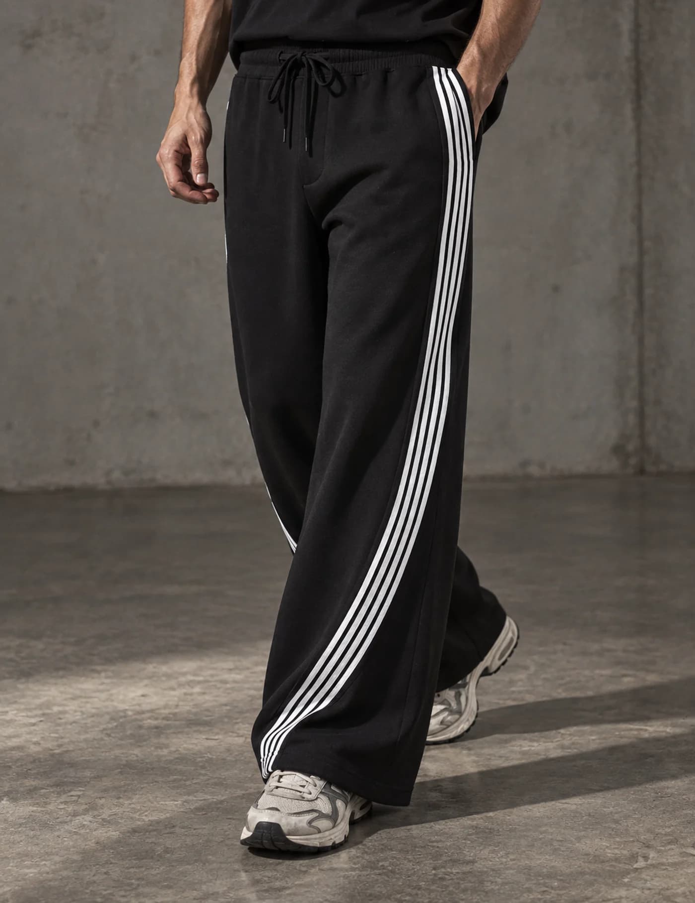 Male model wearing black wide-leg track pants with curved white side stripes