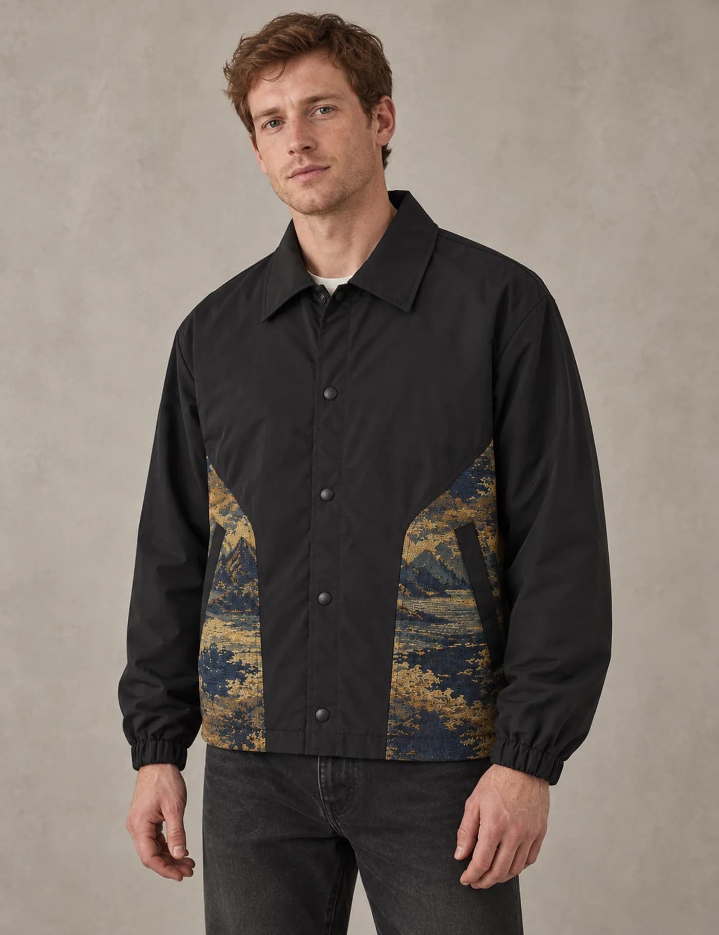 Male model wearing a black coach jacket with gold and navy landscape tapestry panels