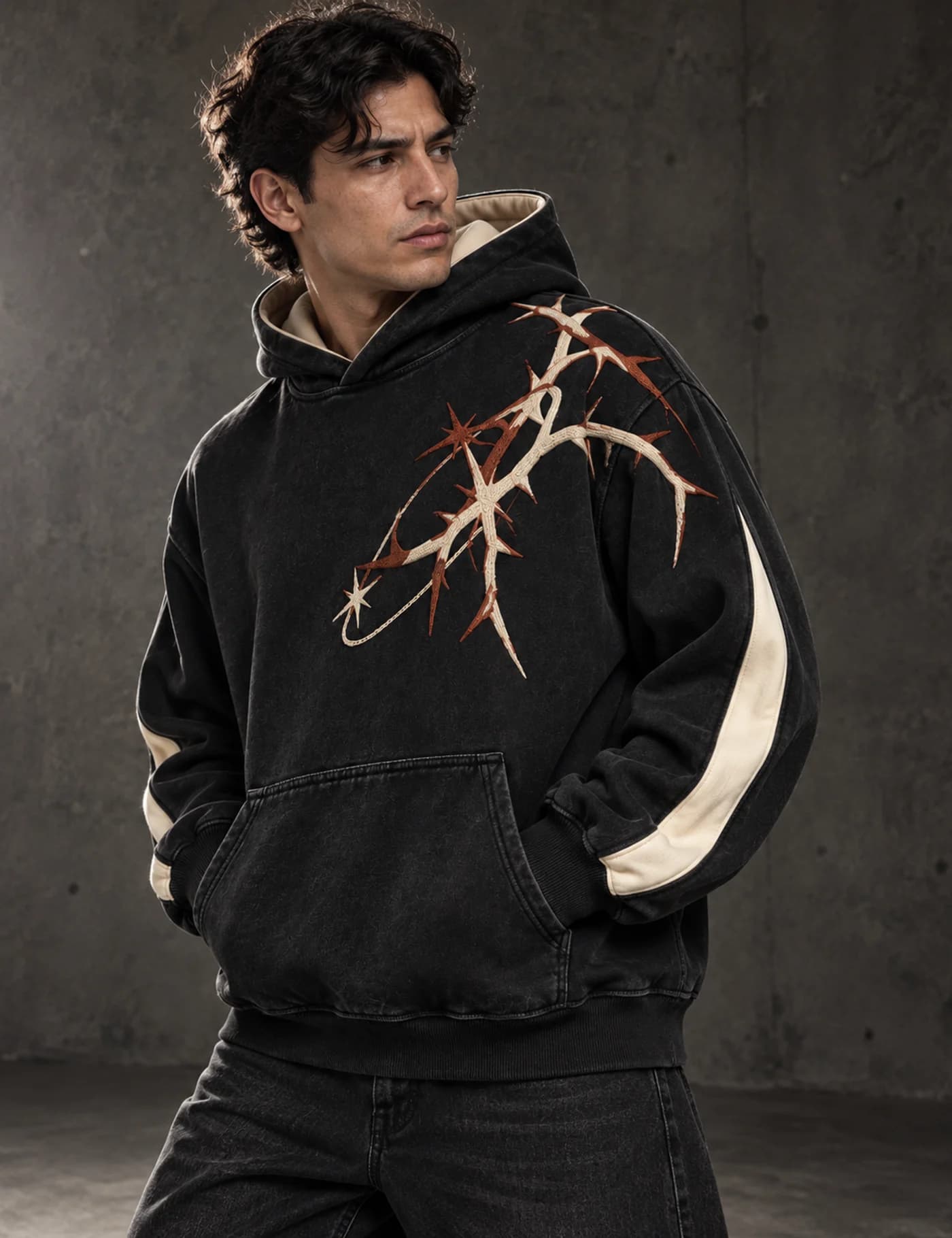 Latino male model wearing a black oversized hoodie with large cream and rust thorn embroidery