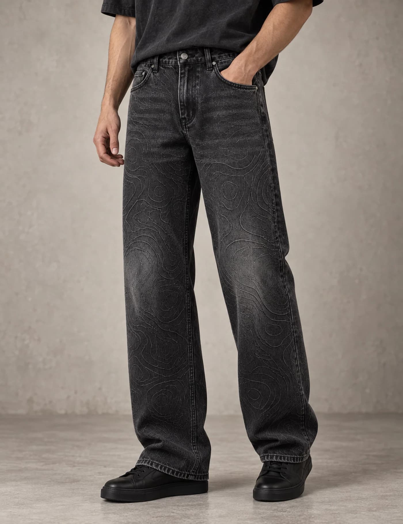 Male model wearing washed black wide-leg jeans with a tonal topographic contour pattern