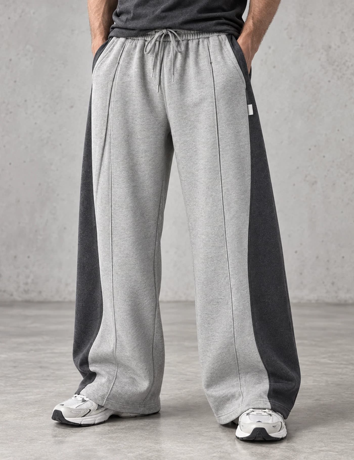 Male lower-body model wearing light gray wide-leg sweatpants with broad charcoal side panels