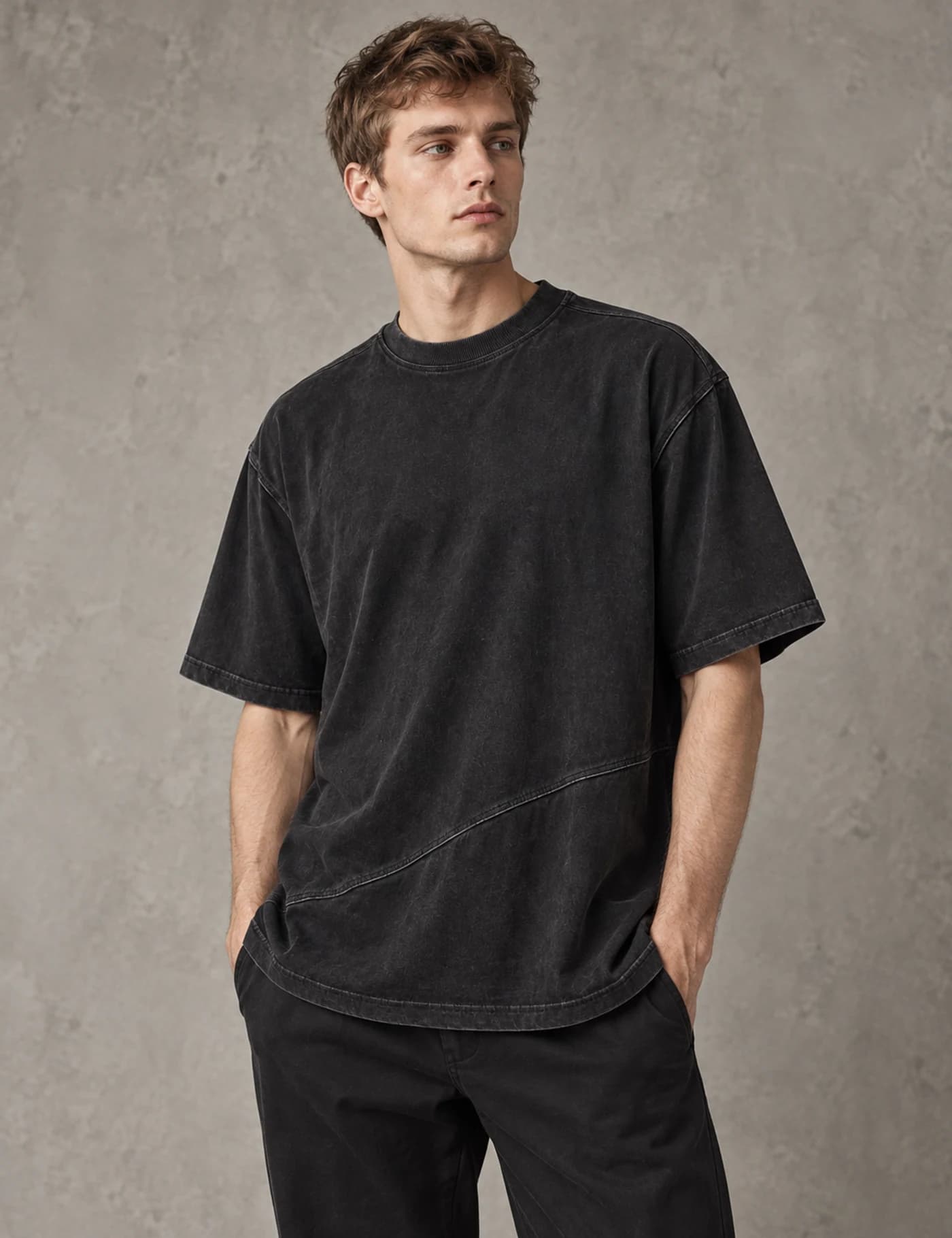 Fair-skinned European male model wearing a washed black oversized T-shirt with a curved diagonal front seam