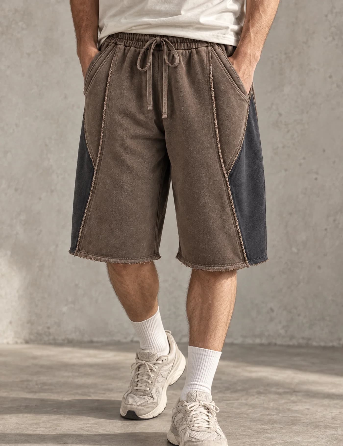 Male lower-body model wearing washed brown long shorts with charcoal curved side panels