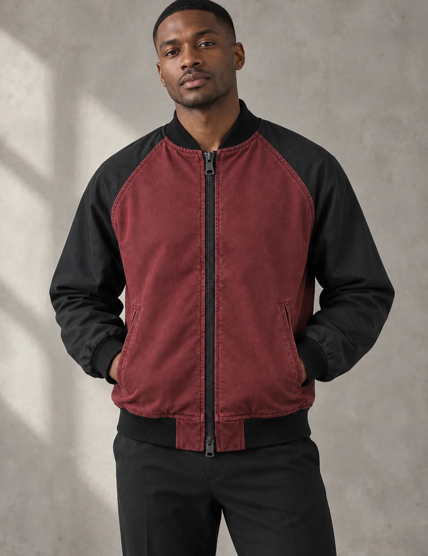 Black male model wearing a washed burgundy bomber jacket with black raglan sleeves